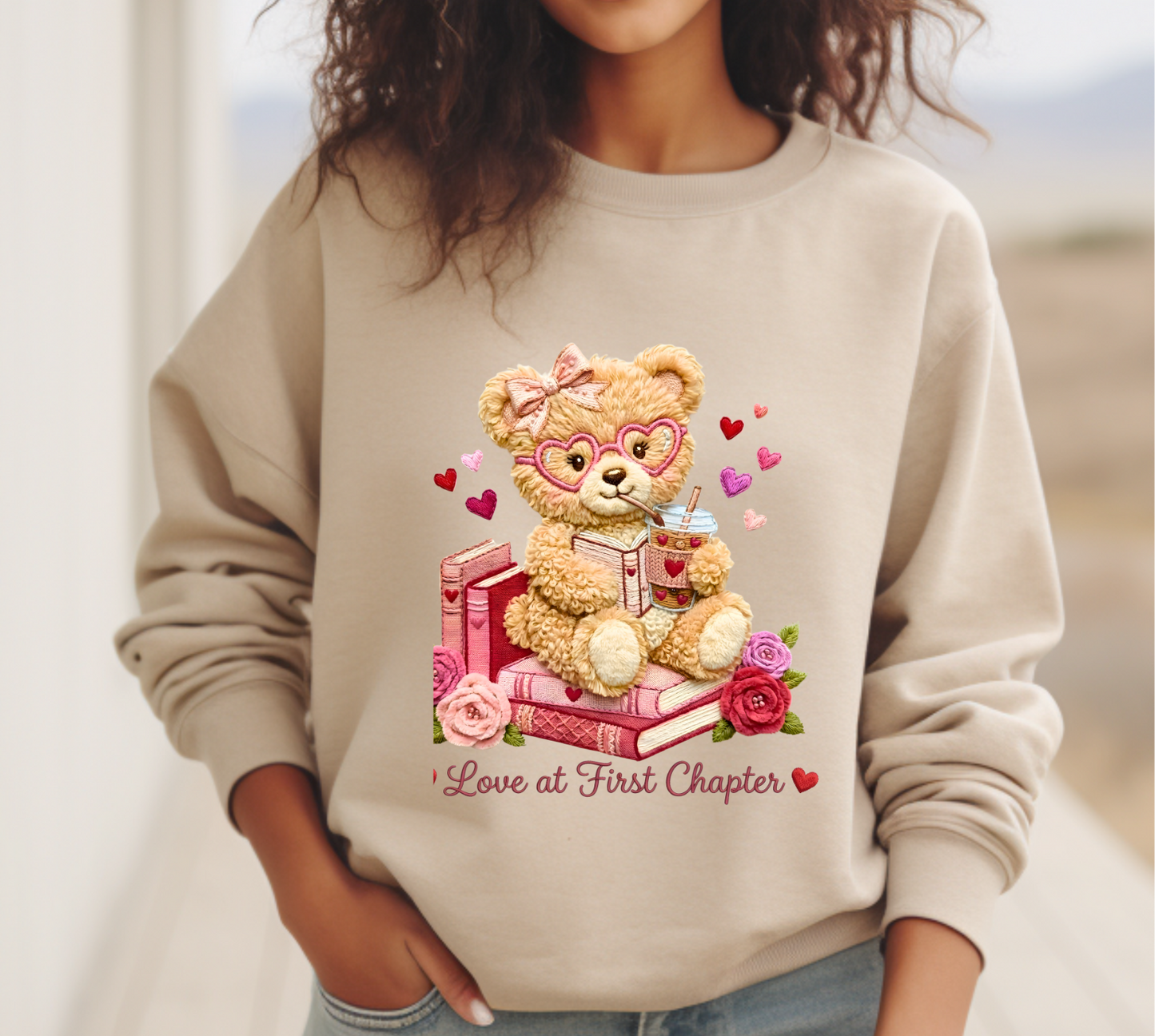 Beige sweatshirt with teddy bear design and text 'Love at First Chapter' worn by a person outdoors.