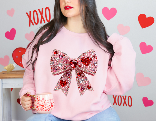 Person wearing a pink sweatshirt with a large bow design, holding a mug, surrounded by heart and 'XOXO' decorations.