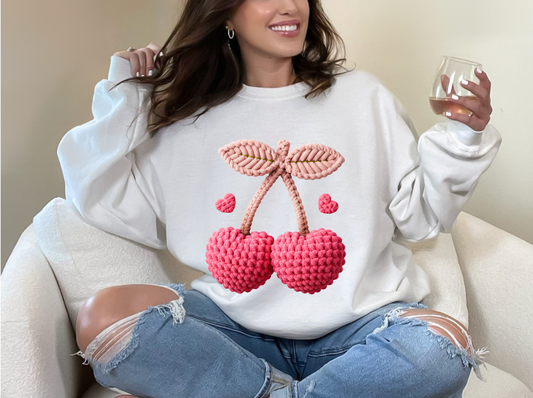 Person wearing a white sweatshirt with cherry design, sitting on a couch.